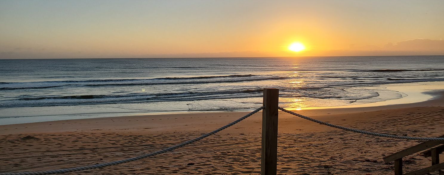 Sunset over a quiet beach with a rope fence